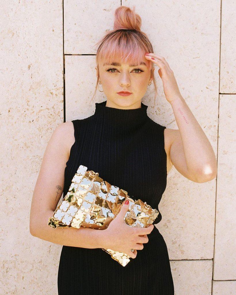 Maisie Williams com cabelo rosa e franja preso em um coque alto