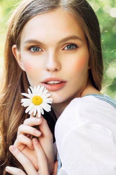 Mulher com cabelos loiros escuros segura flor em suas mãos