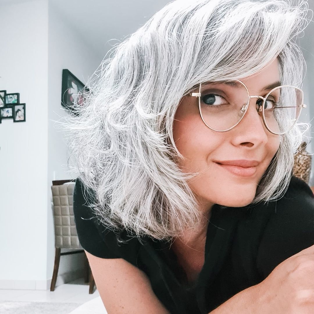 Mulher jovem de cabelo branco e grisalho posa de óculos e blusa preta