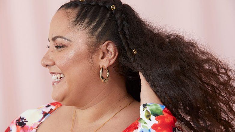 mulher de perfil passa a mão pelo cabelo ondulado e sorri