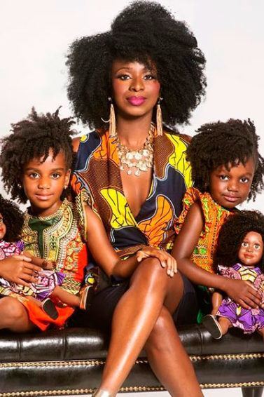 Mulher com cabelo afro e duas meninas que seguram bonecas