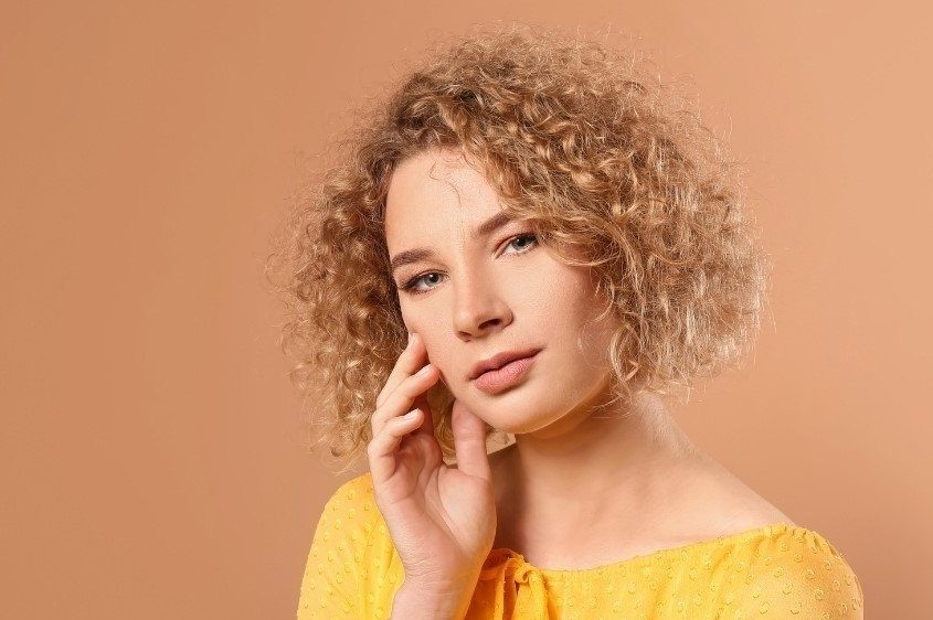 Mulher com cabelo cacheado curto, estilo chanel, e fios loiros