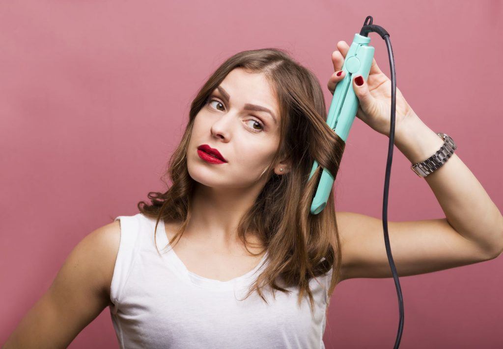 Mulher cacheando os fios com chapinha para cabelo