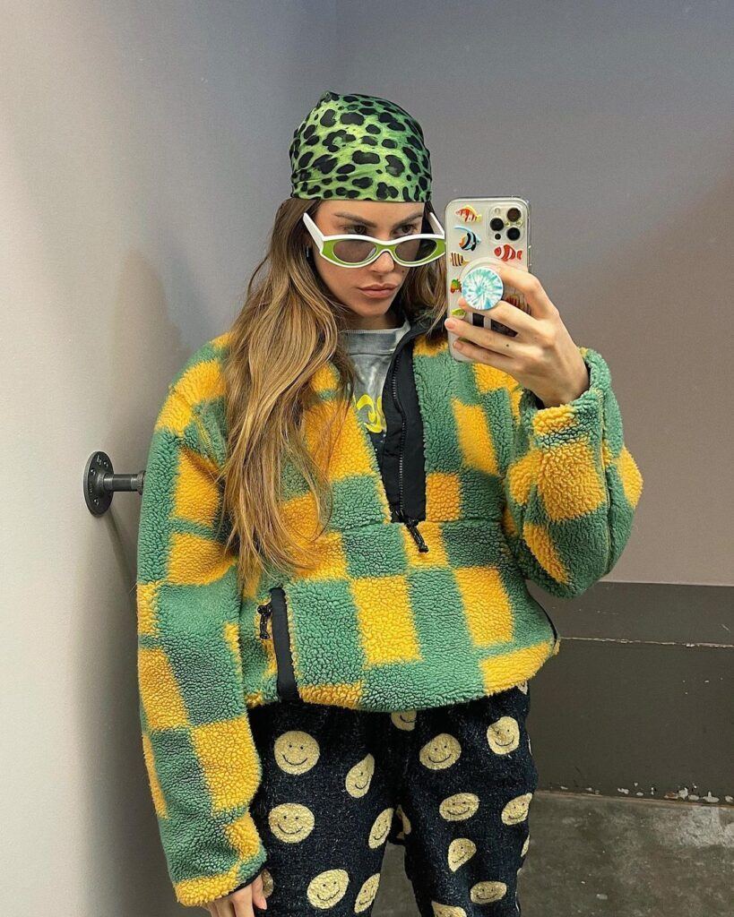 Clara Berry com roupas coloridas e óculos tirando foto no espelho