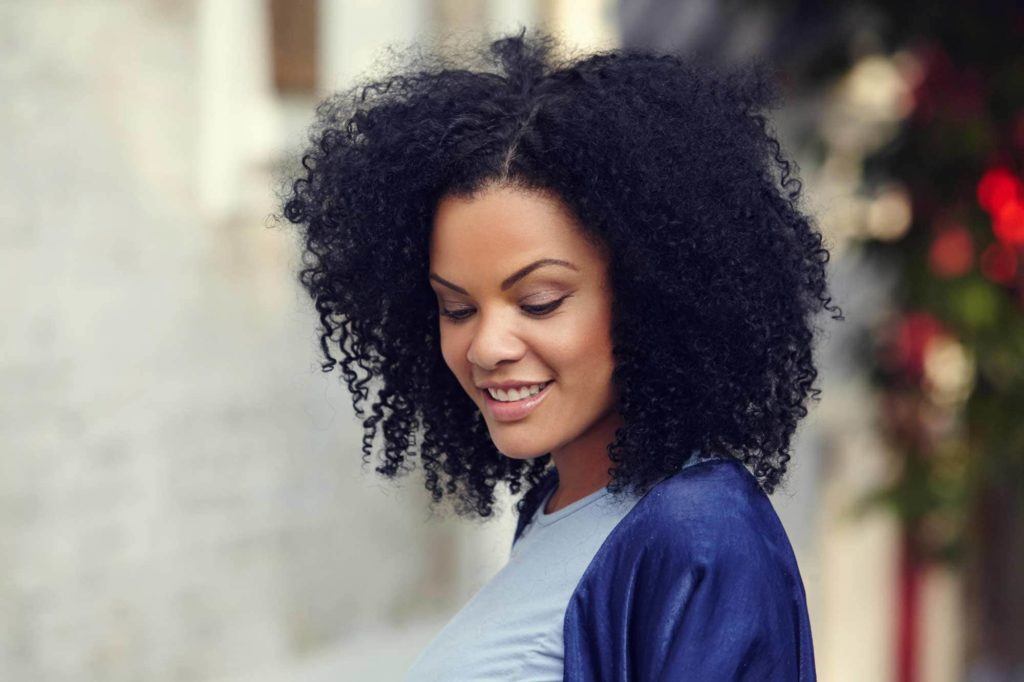 Modelo com cabelo crespo, afro, na altura dos ombros, sorrindo e olhando para baixo