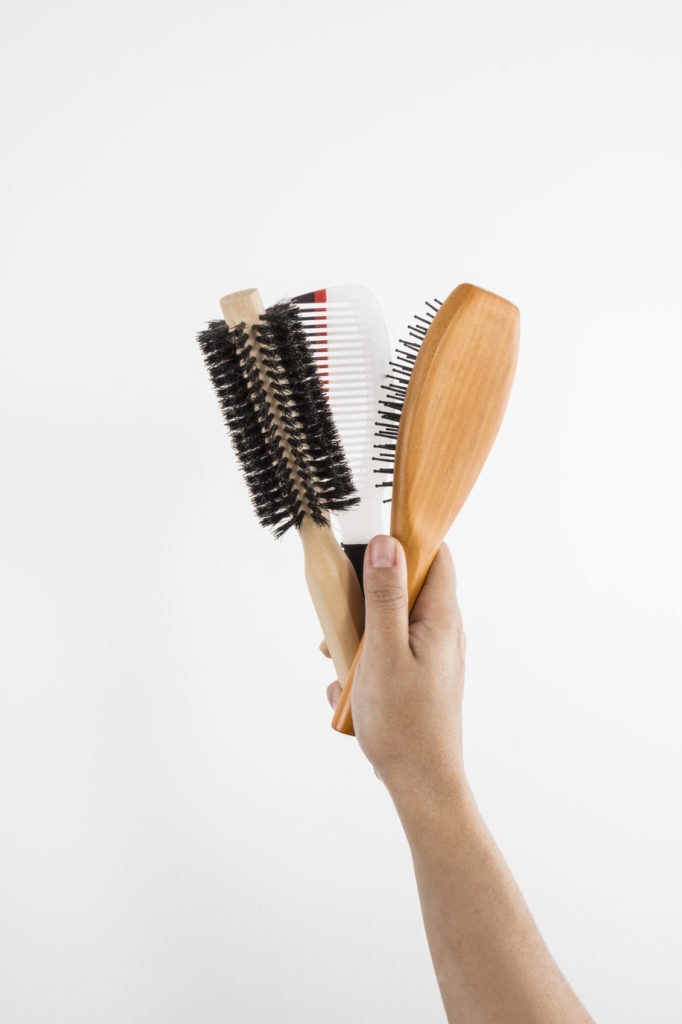 Uma mão mostra três opções de escovas para cabelo masculino