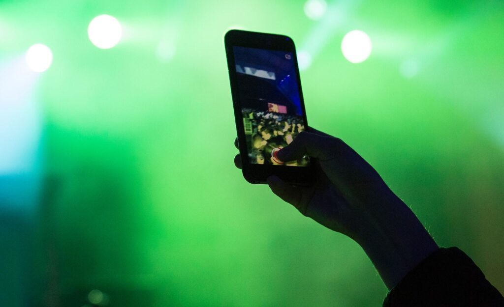 Celular sedo segurado em show de música com luz verde de fundo