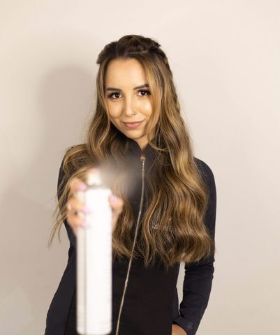 Influenciadora Gabriela Farah com cabelo castanho longo, roupa preta e spray de cabelo