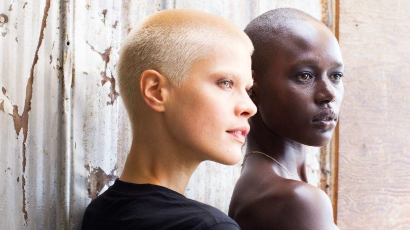 Mulher branca usa buzz cut platinado e mulher negra usa cabeça totalmente raspada.