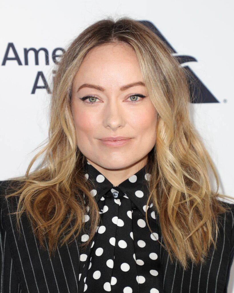 Atriz de rosto quadrado Olivia Wilde com corte de cabelo médio em camadas estilo loiro platinado com luzes ondulado