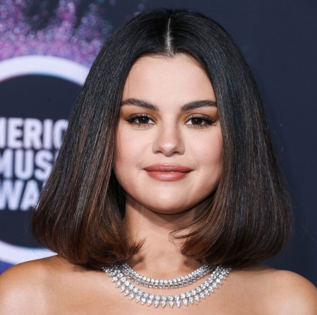 Atriz e cantora de rosto quadrado Selena Gomez com corte de cabelo médio long bob castanho iluminado