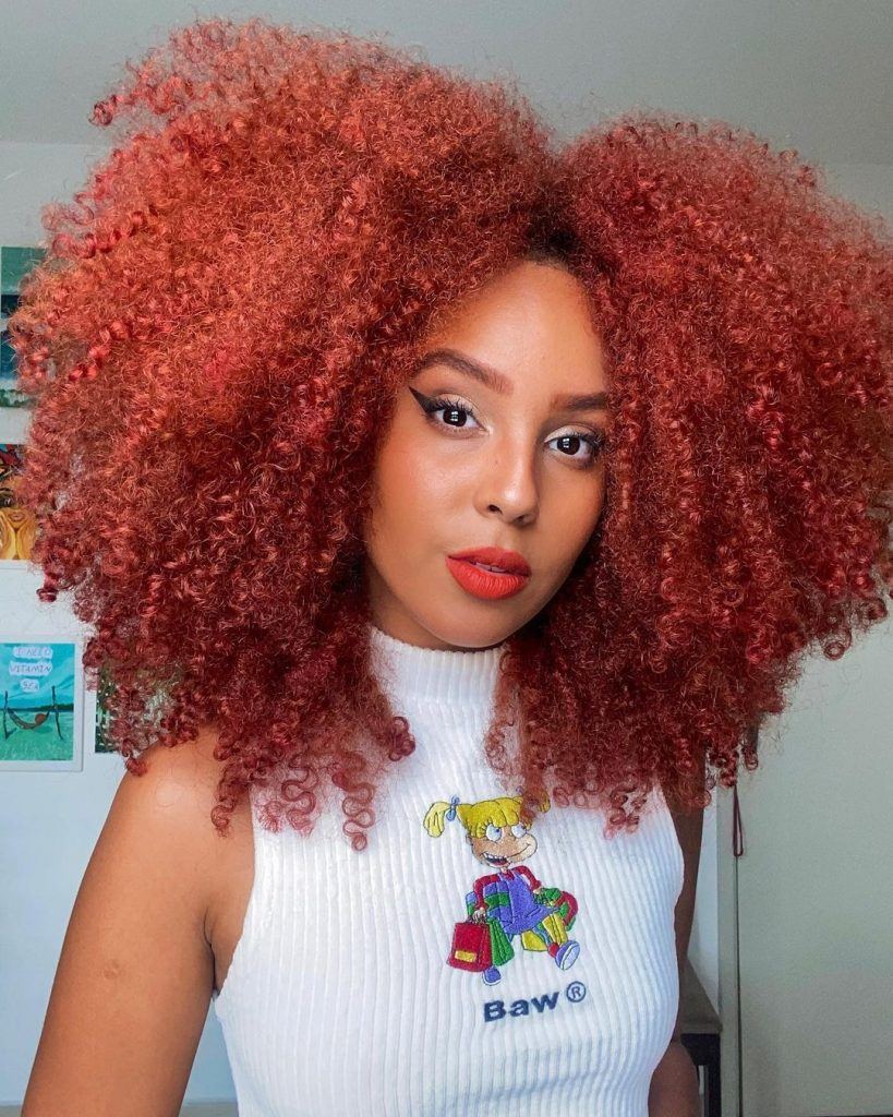mulher com cabelo cacheado vermelho volumoso dividido ao meio
