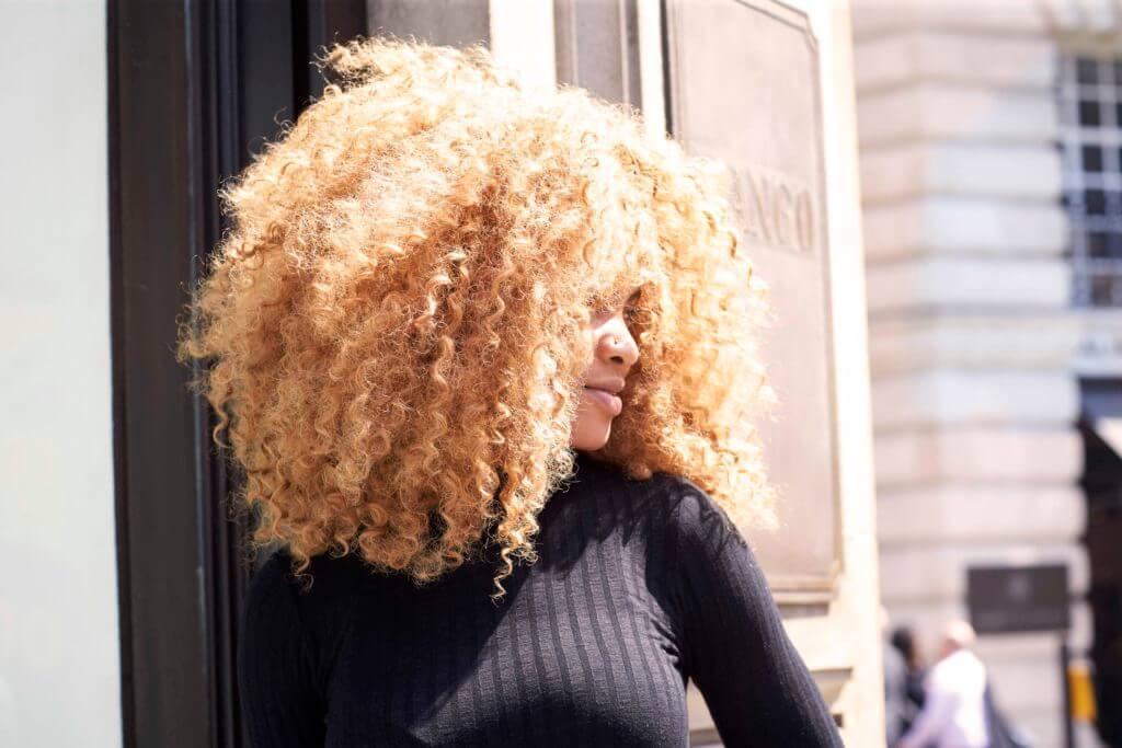 Mulher com cabelo afro loiro volumoso posa
