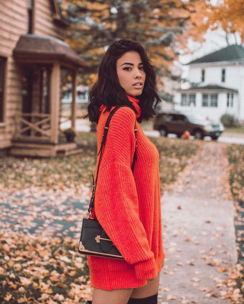 Mulher com cabelo castanh médio com blusa laranja e bolsa preta