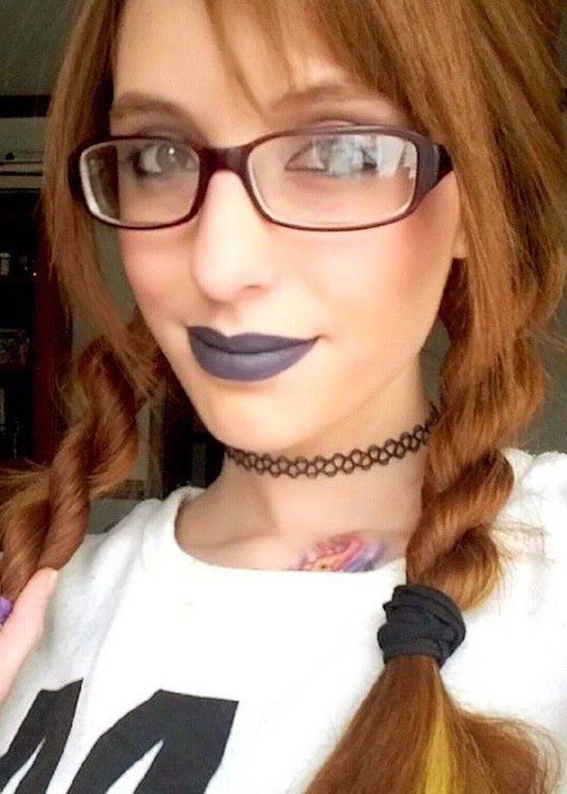 Mulher ruiva usa óculos, veste blusa branca e tem o cabelo com trança enrolada