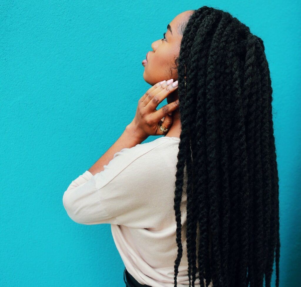 Mulher posa de costas num fundo azul com tranças twist no cabelo preto