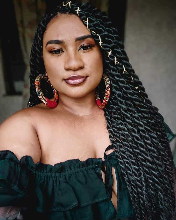 Mulher posa de blusa preta e cabelo longo preto com trança twist grossa