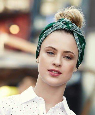 Mulher loira usa camisa branca e lenço verde e ensina a fazer um penteado com bandana cheio de estilo