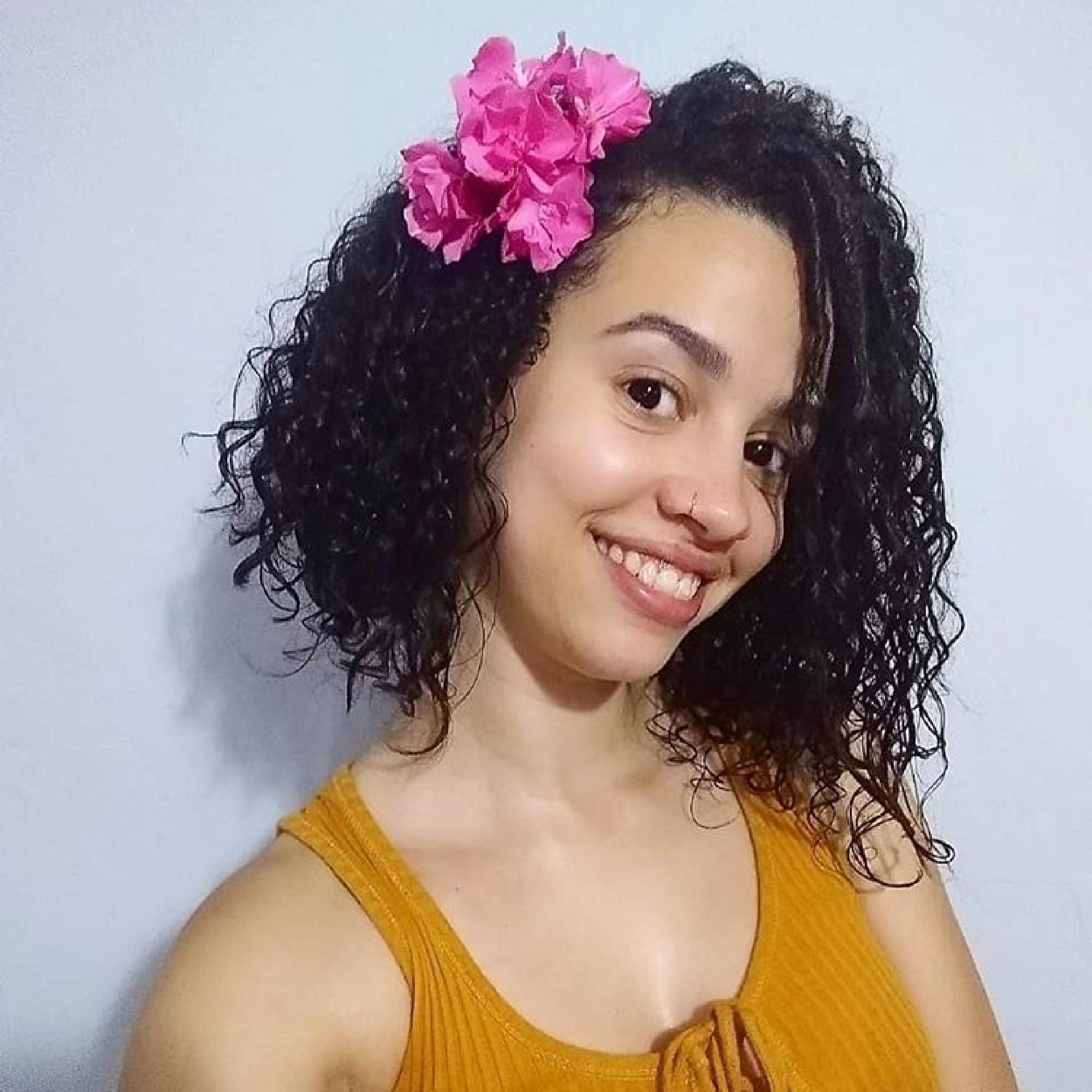 Modelo com cabelo na altura do ombro na lateral enfeitado com flor e blusa regata amarela