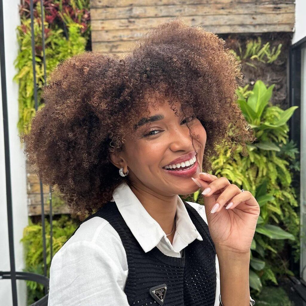Mulher de camisa branca e colete preto exemplificando um dos cortes curtos para cabelos cacheados