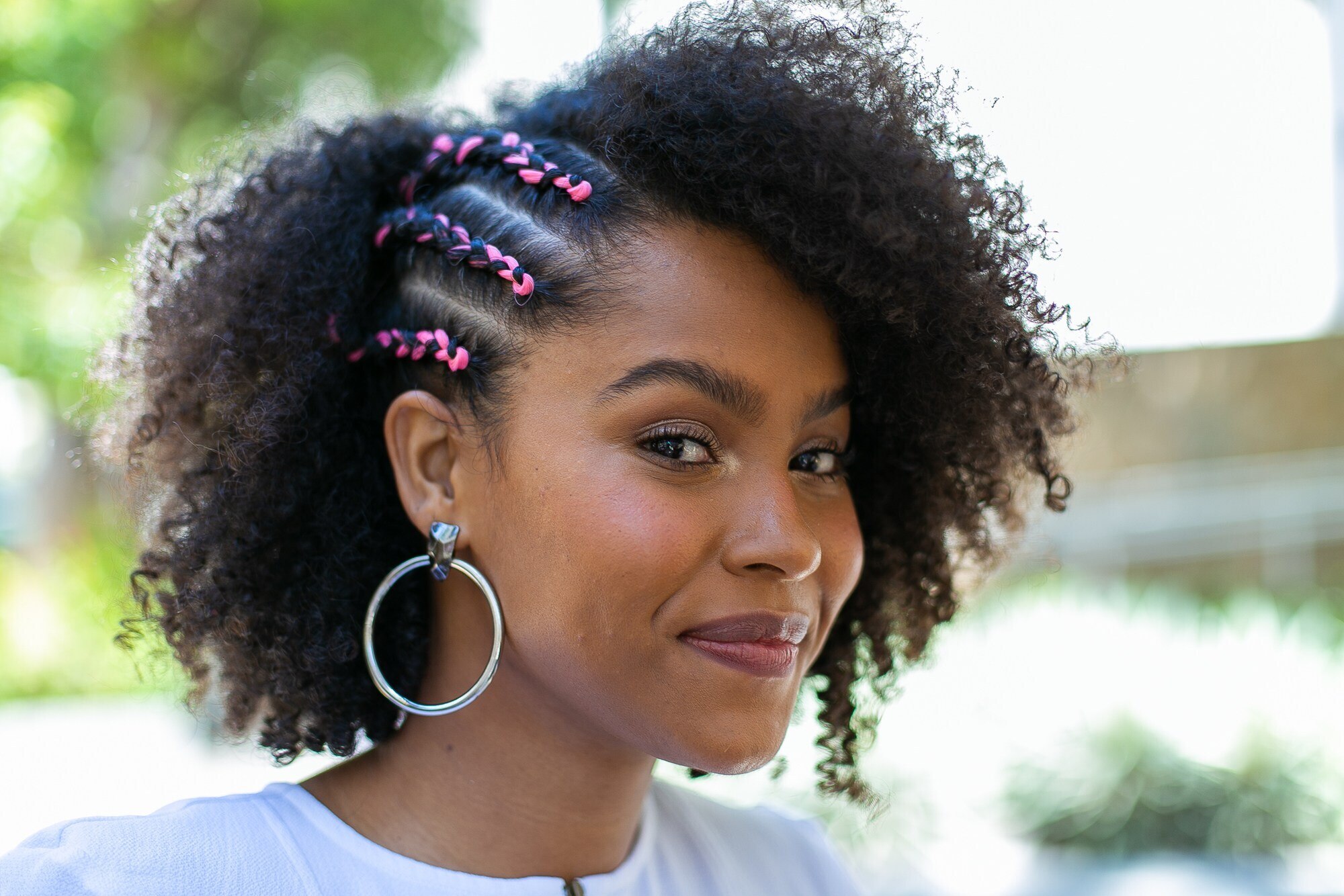 Mulher com cabelo cacheado curto com trancinhas coloridas na lateral direita