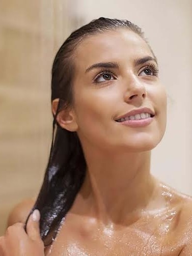 Lavar o cabelo com água mineral: mulher morena tomando banho