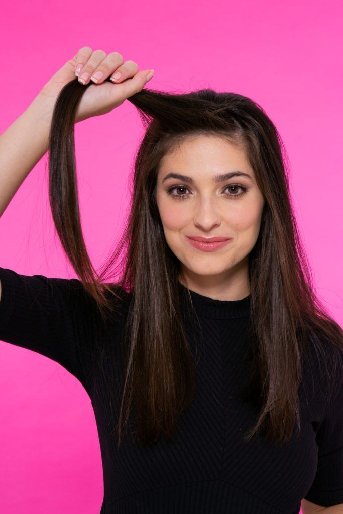 modelo de cabelo preto, liso e longo em fundo rosa separando uma mecha frontal
