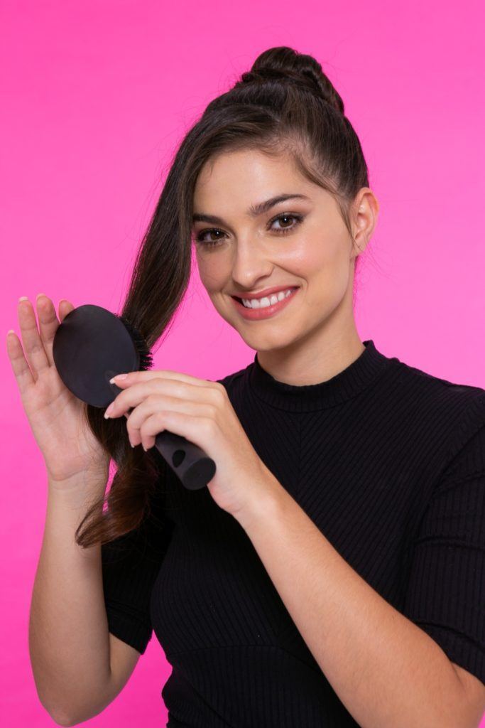 modelo de cabelo preto, liso e longo em fundo rosa com um coque penteando a mecha frontal