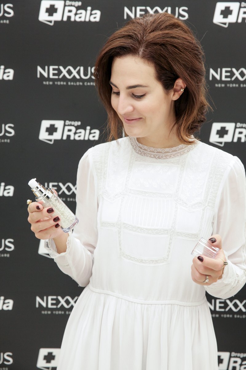 Vic Ceridono segura um produto nas mãos, enquanto posa usando vestido branco