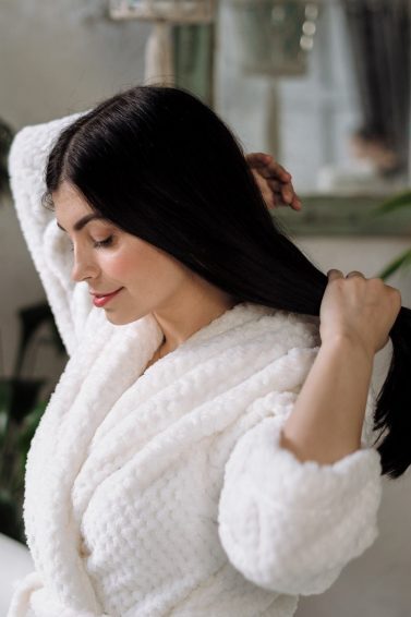 Mulher vestida de roupão passa a mão em seus cabelos longos, lisos e castanhos