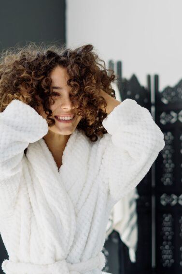 mulher de roupão com as mãos no cabelo cacheado