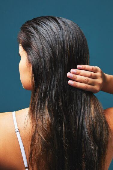 mulher de costas com as mãos em cabelo oleoso