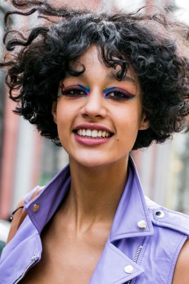 Mulher usa cabelo punk bob nos fios cacheados e veste colete jeans