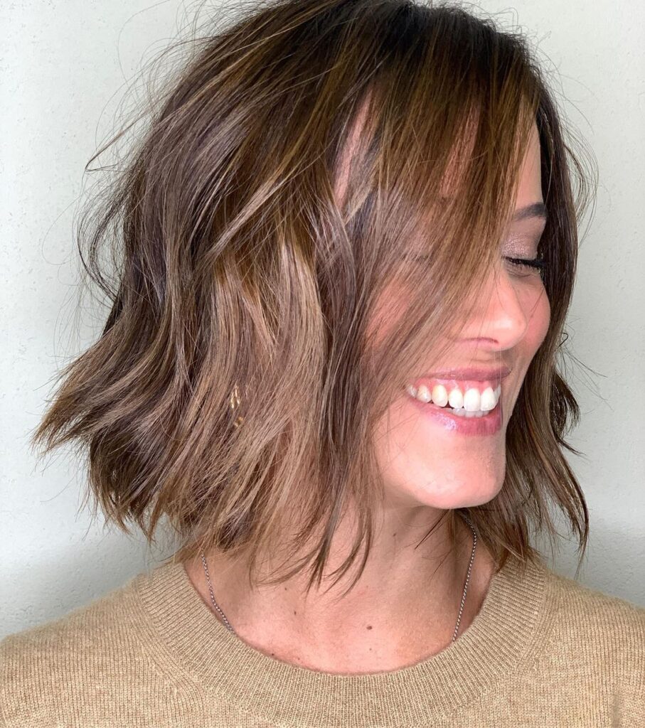 Mulher sorrindo com blusa bege e cabelo castanho claro iluminado chanel
