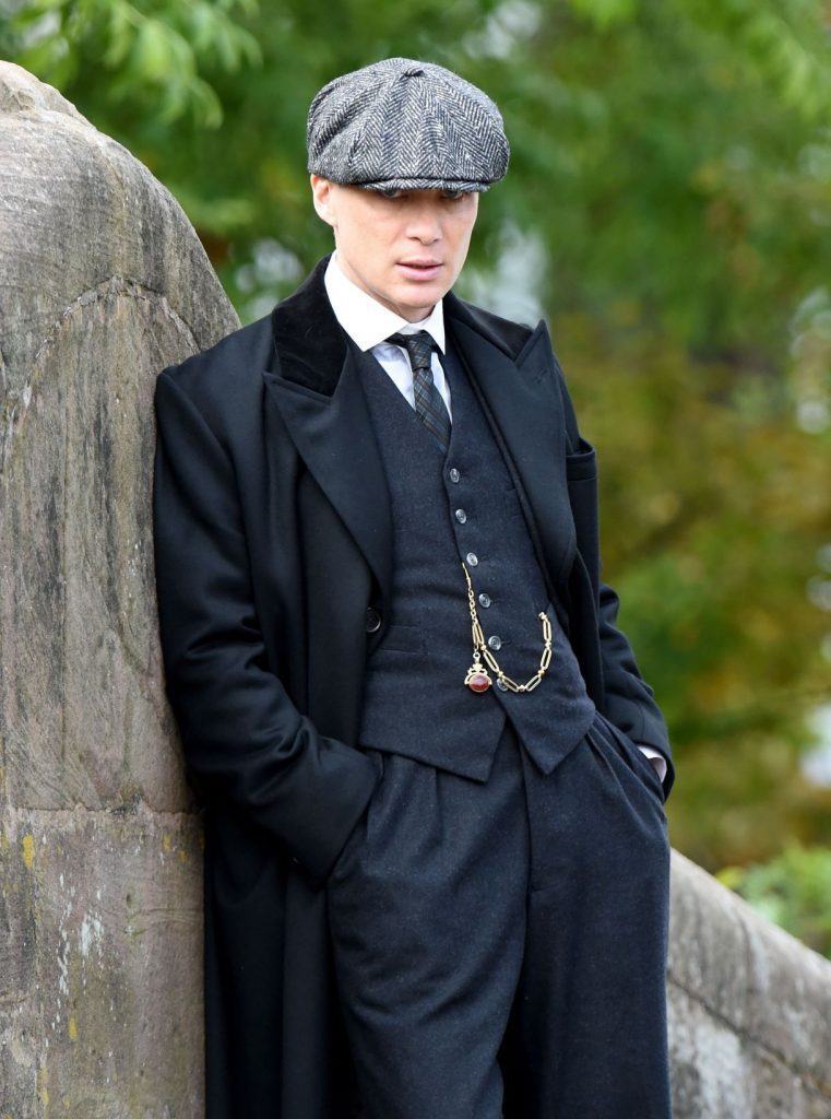 O ator Cillian Murphy caracterizado como Tommy Shelby, da série Peaky Blinders. Ele usa roupas da década de 1920, como terno com colete, boina e relógio de bolso