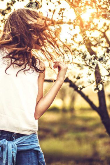 Mulher joga o cabelo de lado, veste blusa branca e calça jeans, e ilustra a matéria sobre Suplemento de vitaminas e aminoácidos para o cabelo