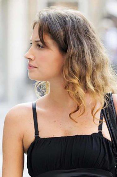Mulher com camiseta preta usa bolsa também preta. Ela tem cabelo ondulado e ilustra matéria sobre cabelo com aspecto de palha