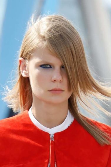 Mulher com cabelo loiro e liso esvoaçante usa casaco vermelho e ilustra matéria sobre cabelo e poluição