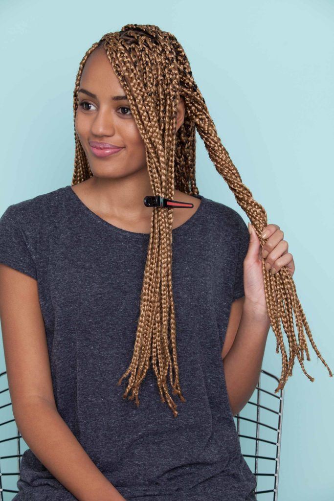 Mulher negra usa camiseta escura e ensina como fazer uma franja com nó duplo em cabelo trançado