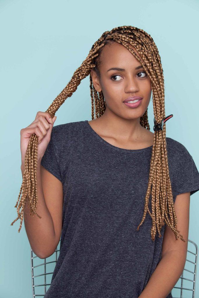 Mulher com cabelo repartido usa blusa escura e ensina como fazer uma franja com nó duplo em cabelo trançado