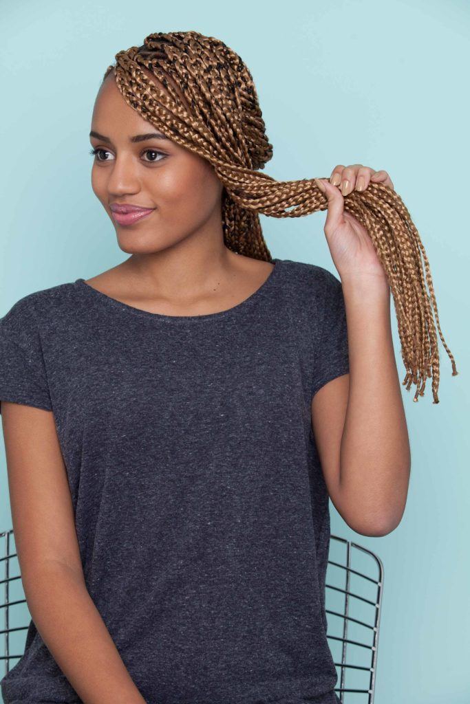 Mulher negra em frente a um fundo azul claro mostra como fazer uma franja com nó duplo em cabelo trançado