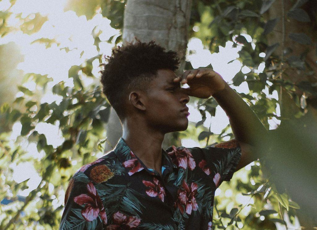 Homem negro de perfil, ao ar livre, com árvores ao fundo. Ele está com uma mão na testa, tentando enxergar ao longe