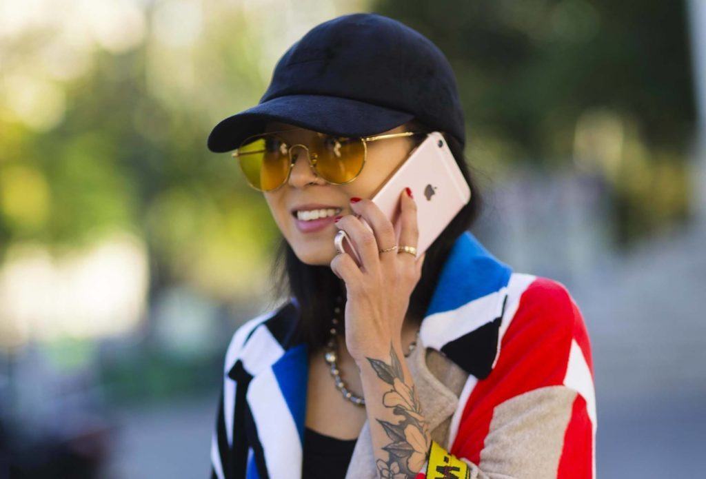 Mulher de cabelos pretos falando ao celular de boné para matéria sobre acessórios de cabelo para o inverno