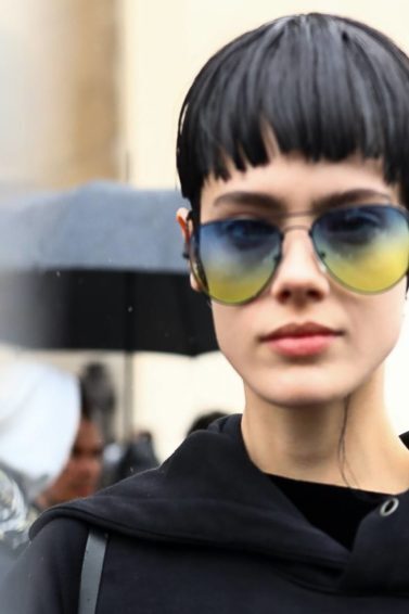 Mulher usa cabelo curto e moletom preto, além de óculos escuros azuis e amarelos