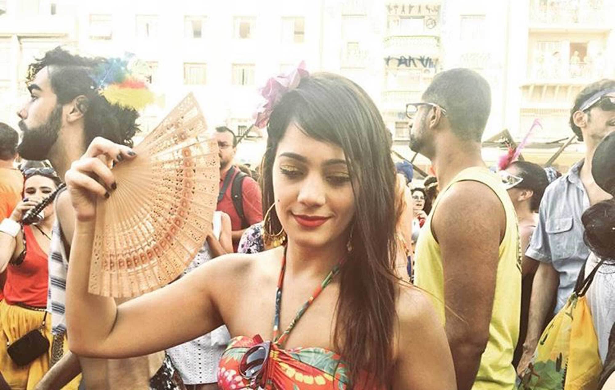 Mulher usa flor no cabelo e top colorido, no meio do bloquinho, e ilustra matéria sobre cabelos de outros carnavais
