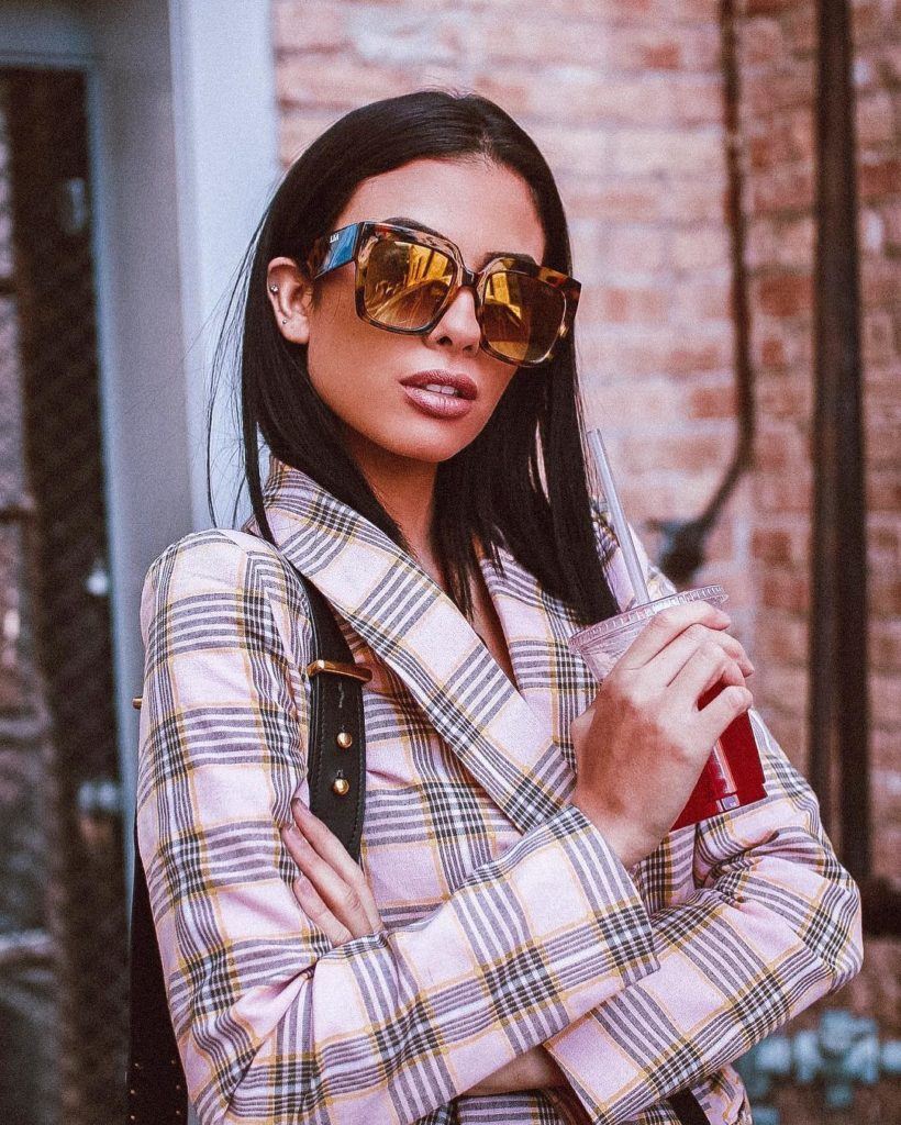 Mulher de cabelo castanho liso no ombro com óculos escuros quadrados e blazer xadrez