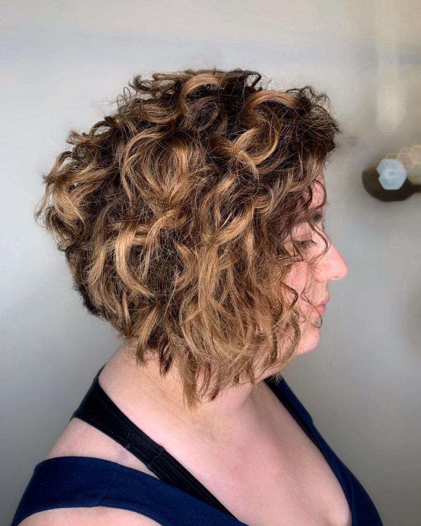 Mulher posa de perfil destacando o corte de cabelo chanel de bico em fios ondulados com luzes
