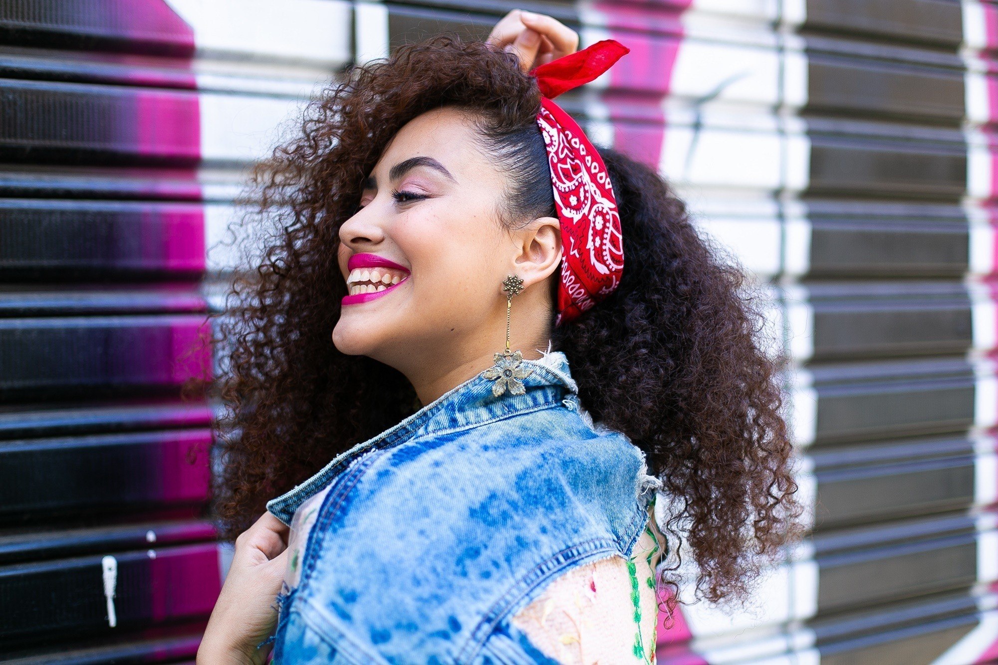 Modelo com cabelo cacheado longo dividido na lateral e com bandana na cabeça