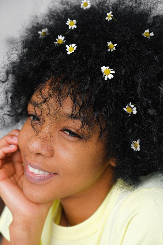 Mulher de cabelos crespos em transição. Ela tem pequenas flores enfeitando os fios