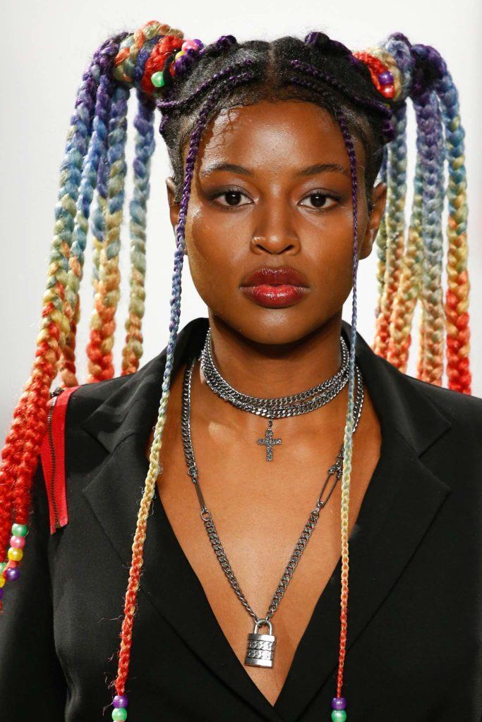 Mulher com cabelos crespos longos e presos em um coque duplo com trancinhas de diversas cores, como vermelho e azul